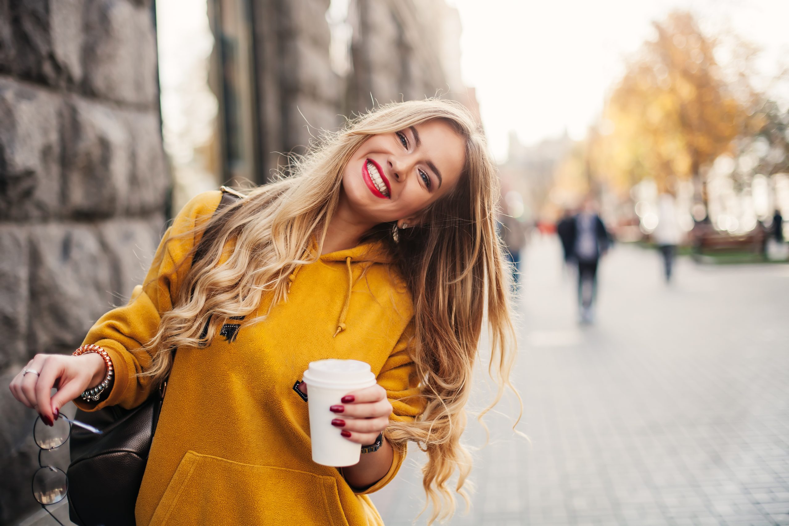 young woman in a yellow sweater holding a coffee and smiling, showing off new white teeth