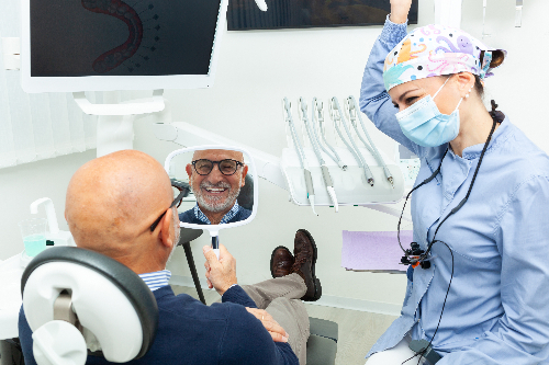 older man smiling in a mirror, happy with new dental implant