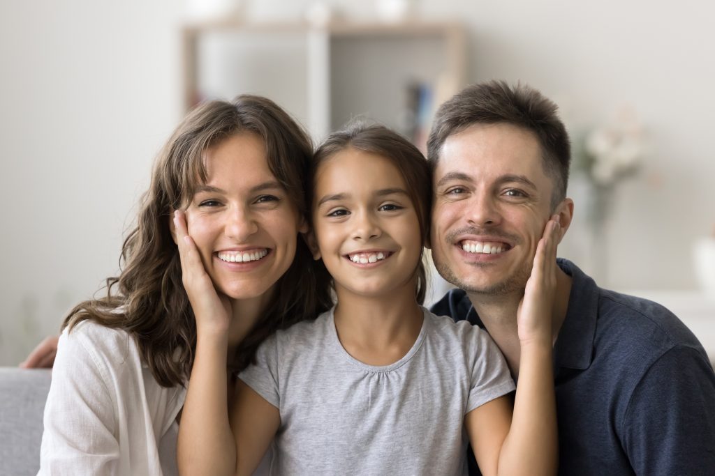 mother and father flanking their smiling daughter, healthy white smiles
