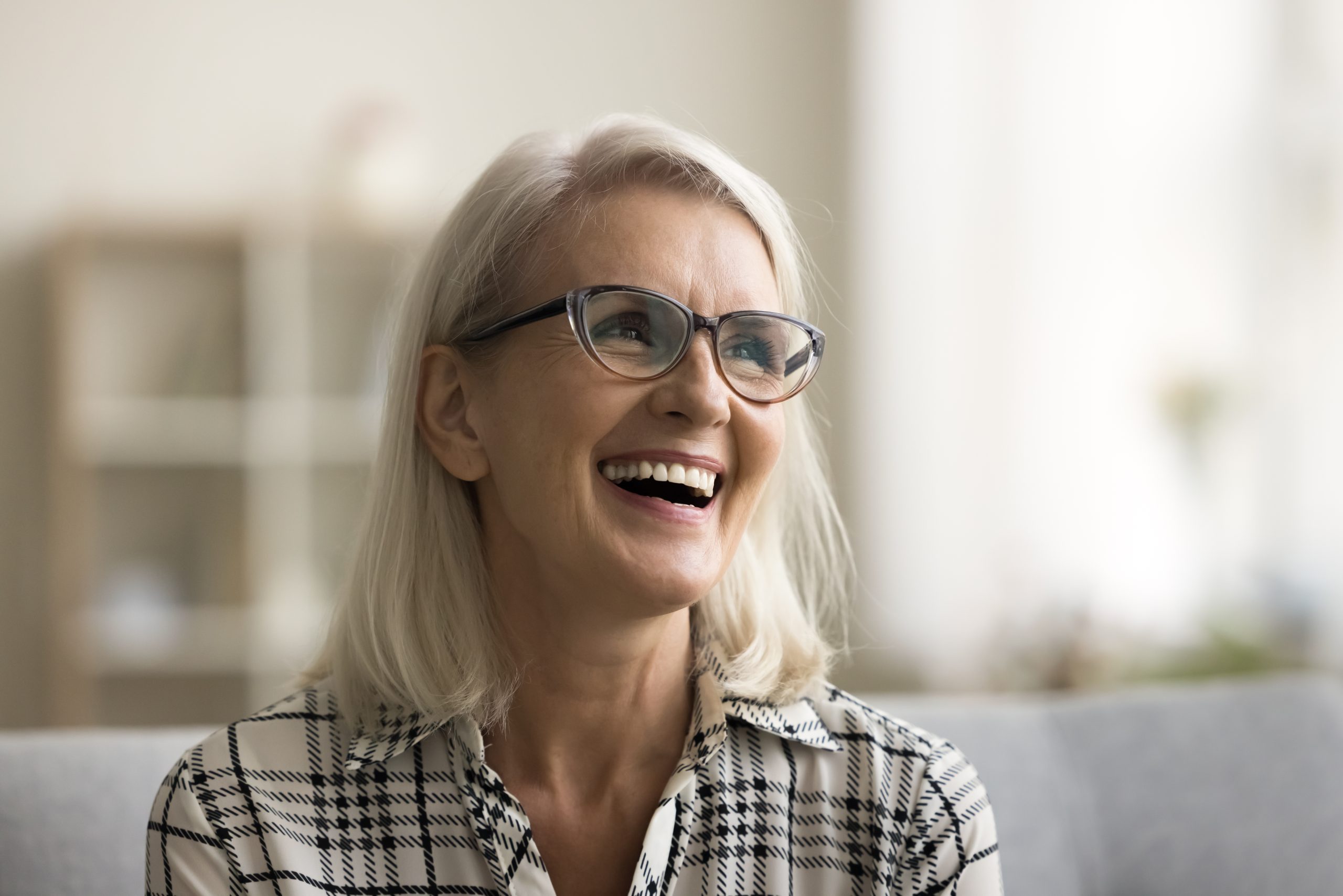 older woman sitting on a couch smiling, new dental implants