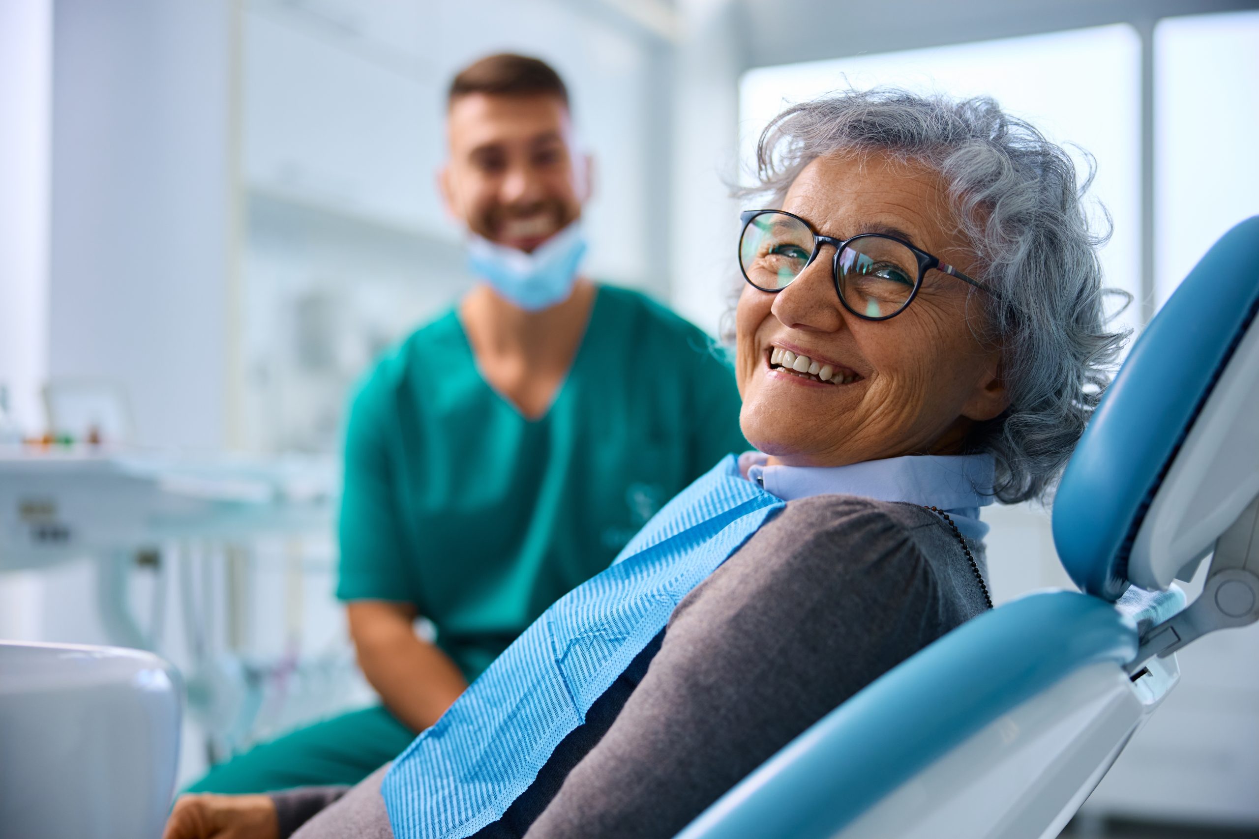 Happy senior woman at dental clinic looking at camera. Her dentist is in the background